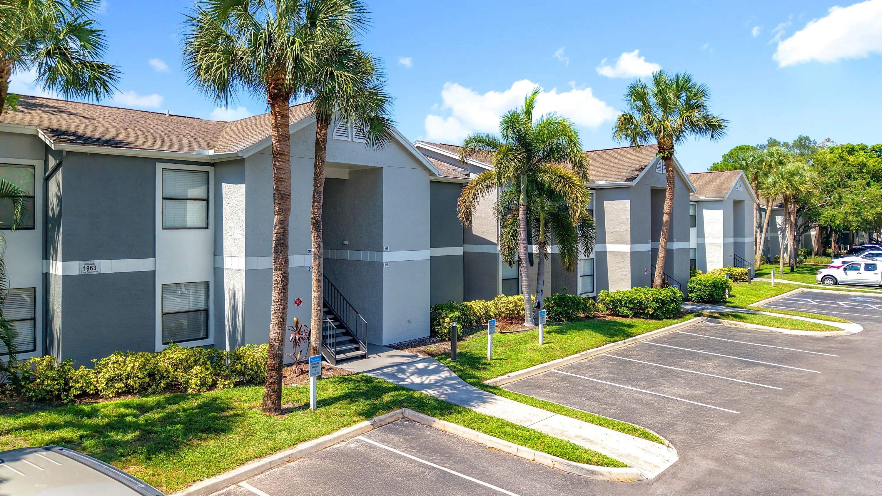 Enjoy vibrant Florida living at River Reach Apartments in Naples. This exterior showcases clean architecture, palm-lined walkways, and plenty of on-site parking.
