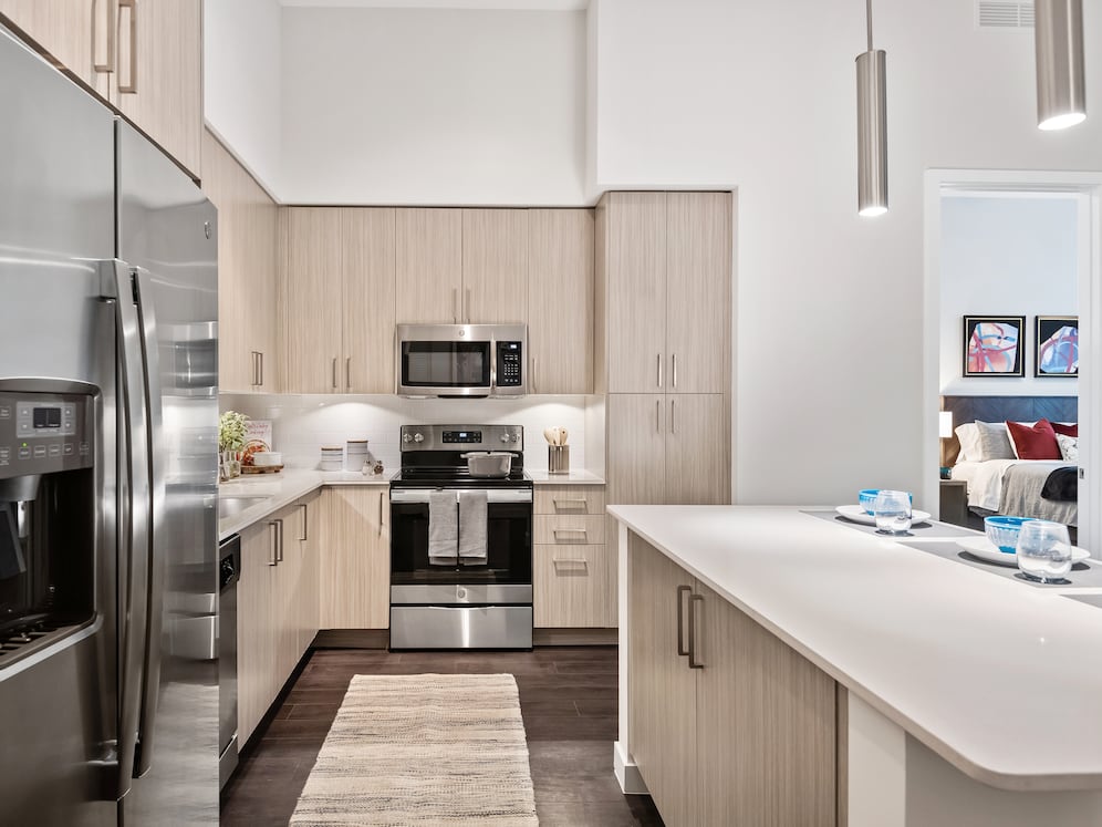 Kitchen with oak cabinetry, undercabinet lighting, white quartz countertops, stainless steel appliances, and hard-surface vinyl plank flooring
