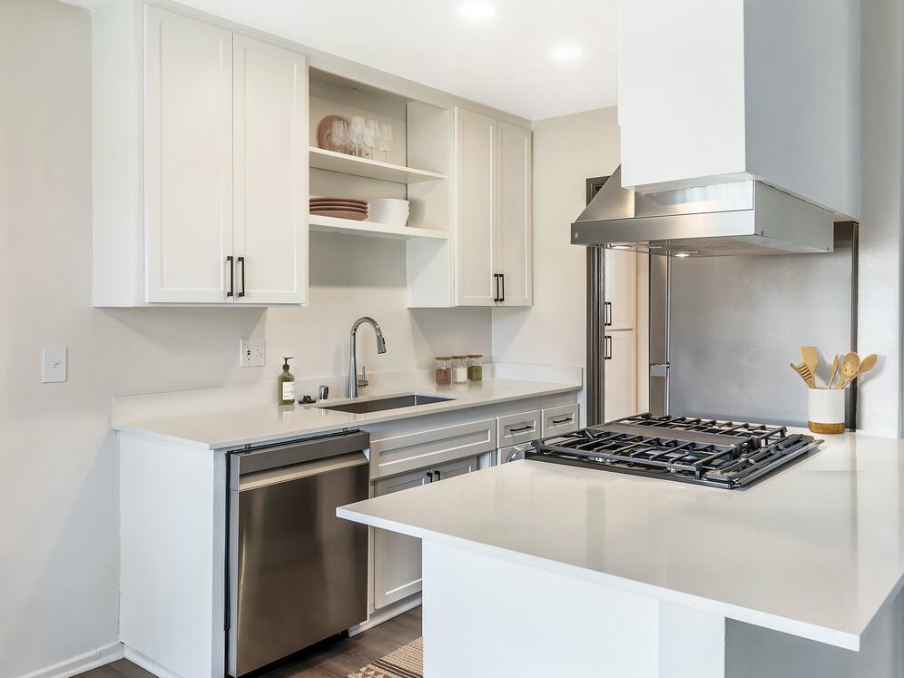 Renovated Package I kitchen with stainless steel appliances, white quartz countertops, white cabinetry, and hard surface flooring (select homes)
