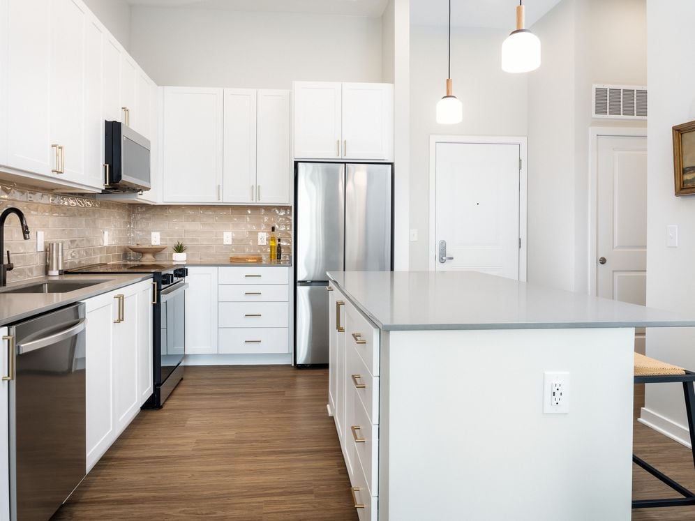 Design Collection I kitchen with white cabinetry, beige tile backsplash, grey quartz countertops, pendant lighting and hard surface flooring