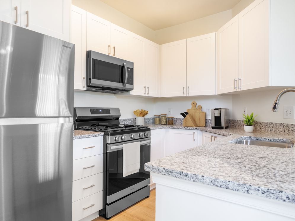 Renovated Package I kitchen with white cabinetry, grey granite countertops, stainless steel appliances, and hard surface plank flooring