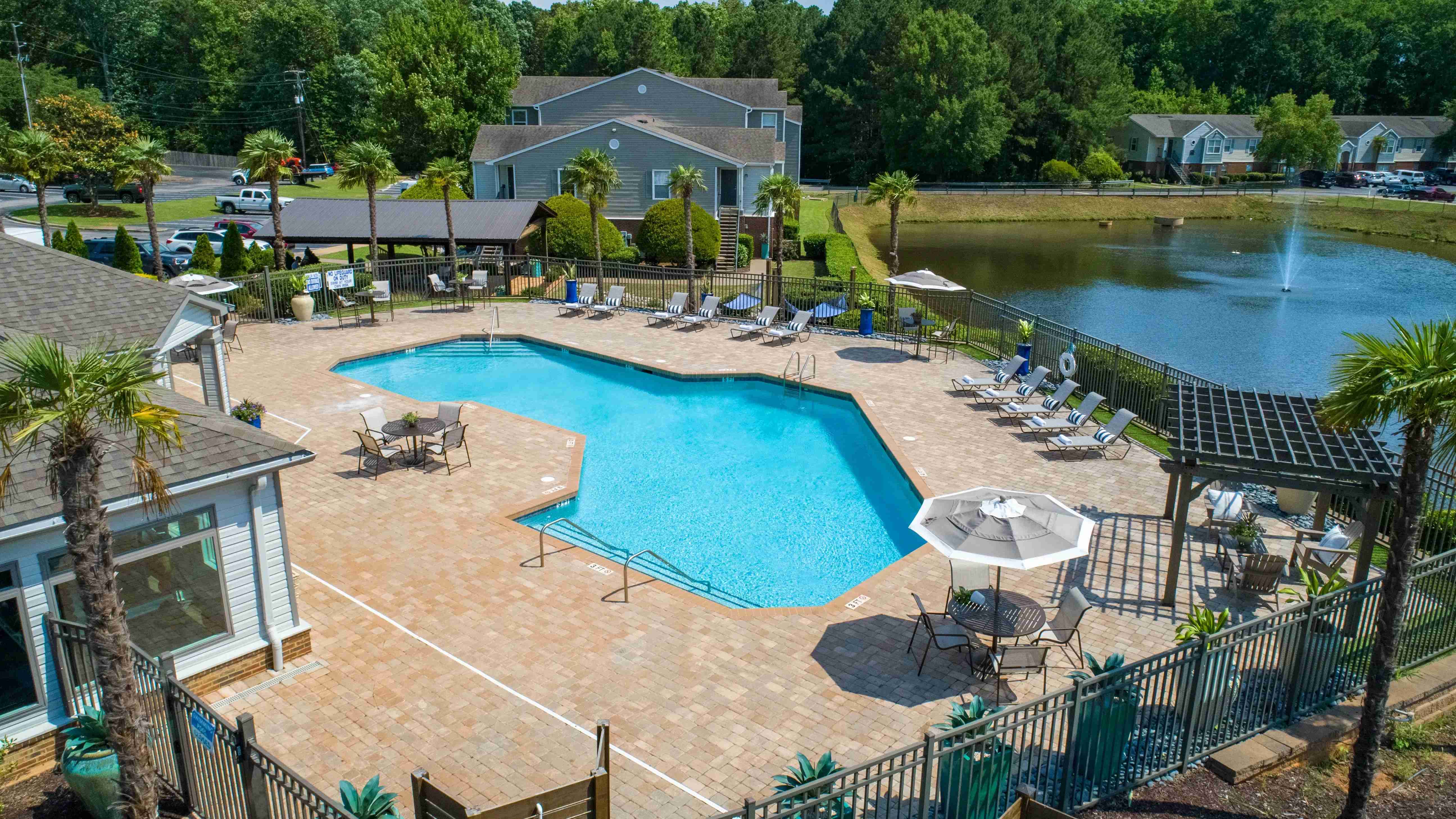An aerial view showcases our gleaming pool, lush greenery, and serene lakeside charm. 
