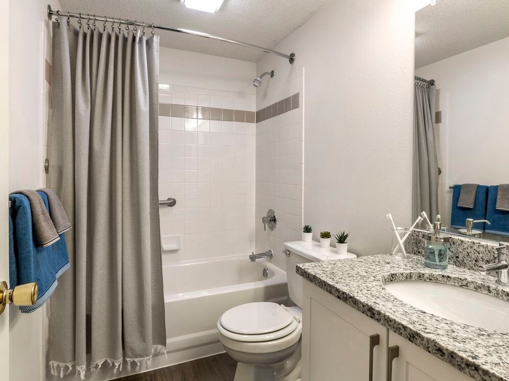 Renovated Package III bath with white cabinetry, grey granite countertops, and shower and bath with tile backsplash