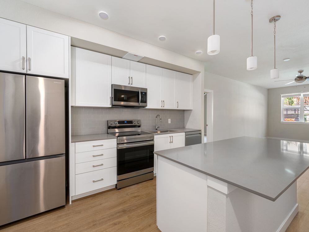 Finish Package I Kitchen with white cabinetry, grey quartz countertops, grey tile backsplash, stainless steel appliances, and hard-surface vinyl plank flooring