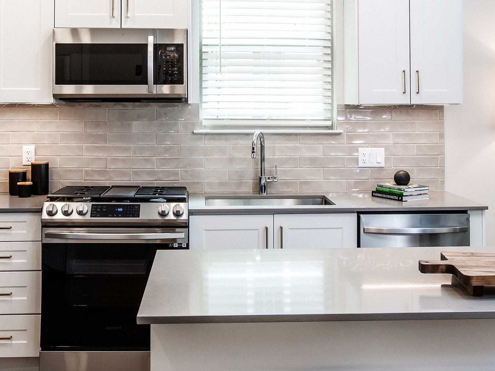 Design Collection II (South Building) Kitchen with white cabinetry, gold pulls, beige tile backsplash, grey quartz countertops, stainless steel appliances, and hard surface flooring