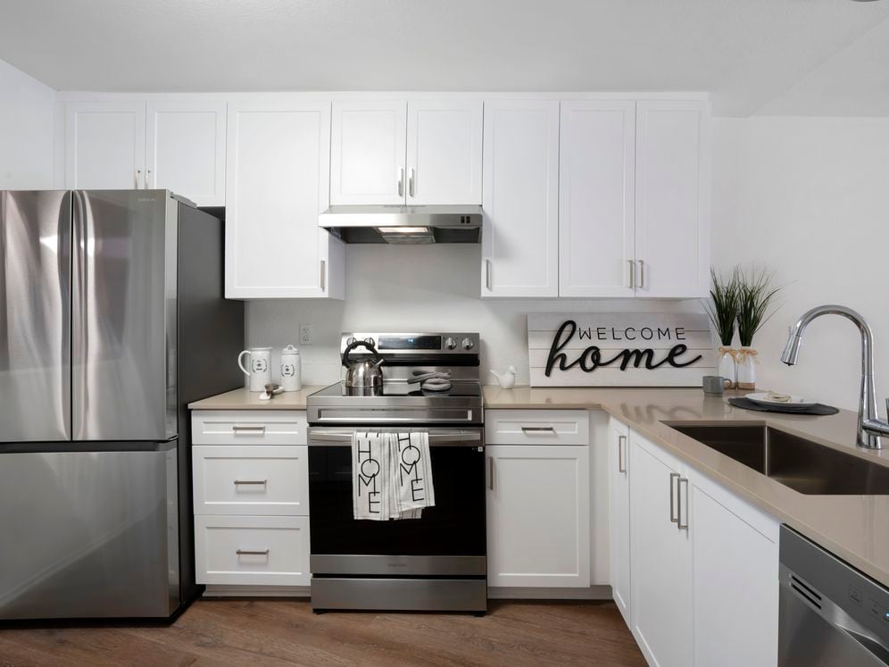Renovated Package I kitchen with stainless steel appliances, light grey quartz countertops, white cabinetry, and hard surface flooring