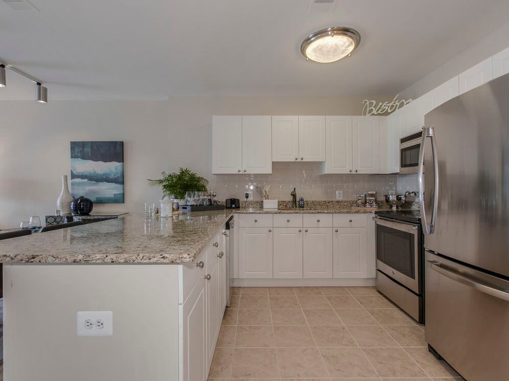 Open concept kitchen with white cabinetry, cream tile backsplash, stainless-steel appliances, granite countertops and hard surface flooring