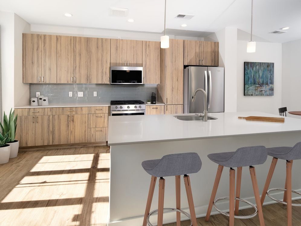Upgrade Scheme townhome kitchen and dining areas with oak cabinetry, grey tile backsplash, grey quartz countertops, stainless steel appliances, and hard surface flooring
