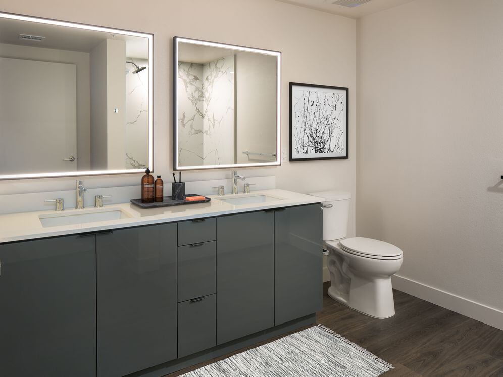 Upgrade Package Bath with grey cabinetry, white quartz countertop, marble shower surround, and lit vanity mirror