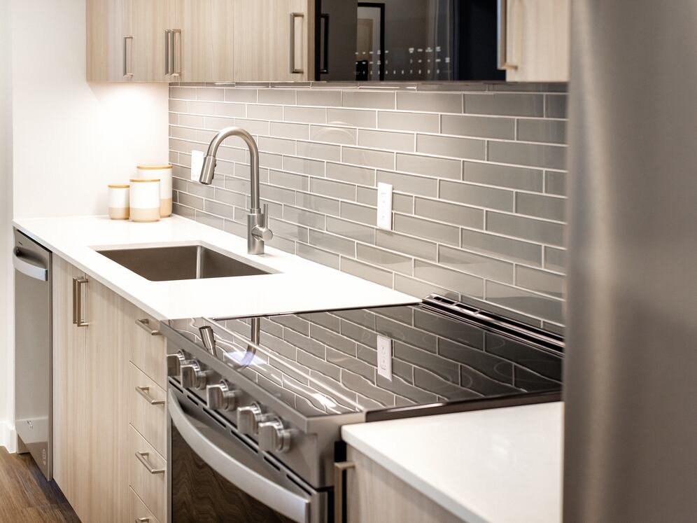 Upgrade Collection I kitchen with light wood cabinetry, grey tile backsplash, white quartz countertops, and stainless steel appliances