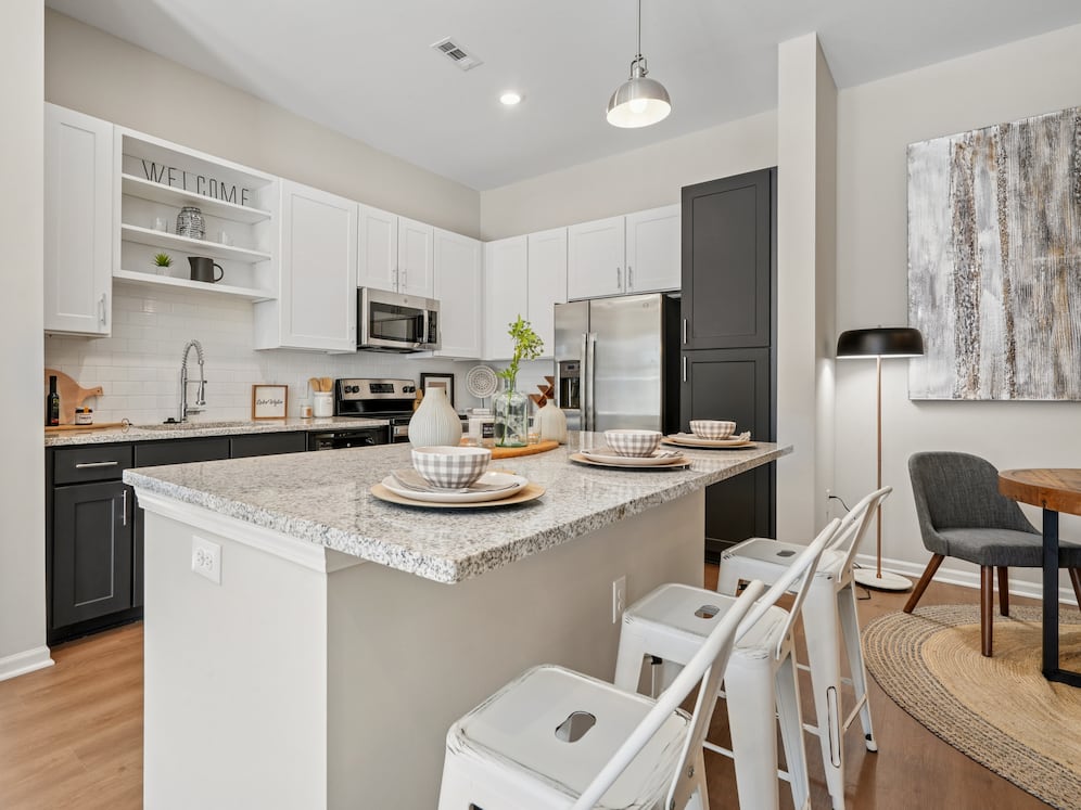 Kitchen with white and dark cabinetry, speckled granite countertops, white subway tile backsplash, stainless steel appliances, and hard surface flooring