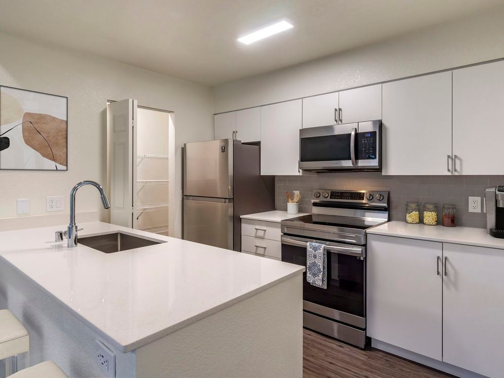 Renovated Package I kitchen with stainless steel appliances, cream quartz countertops, white cabinetry, grey tile backsplash, and hard surface flooring.
