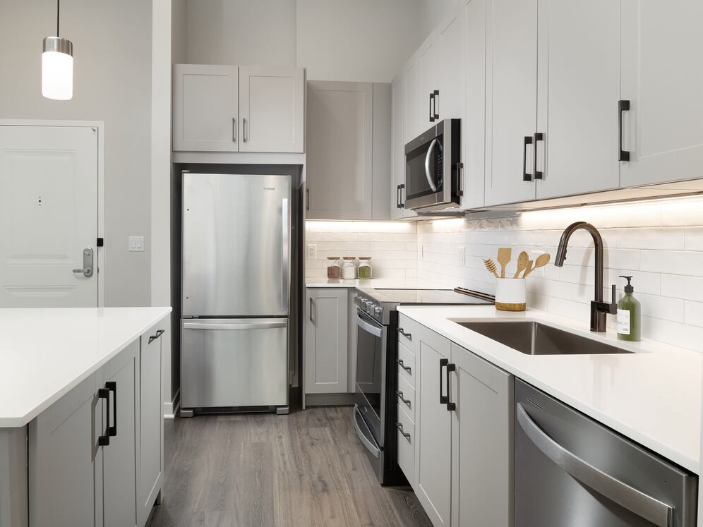 Upgrade Collection II kitchen with stainless steel appliances, grey cabinetry, white quartz countertops, tile backsplash, under-cabinet lighting, and hard-surface flooring