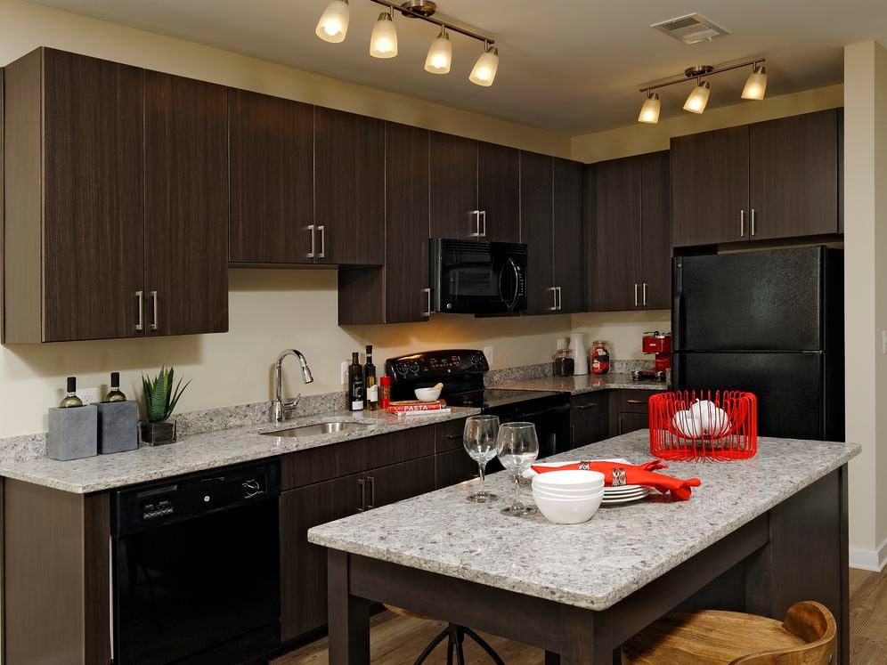 Contemporary kitchen with espresso cabinetry, grey speckled granite countertops, black appliances, and hard surface flooring