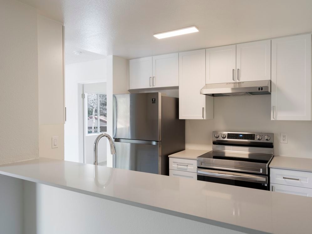 Renovated Package I kitchen with stainless steel appliances, light grey quartz countertops, and new white cabinetry