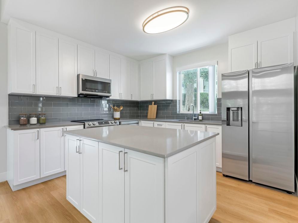 Freestanding Home kitchen with white cabinetry, grey quartz countertops, grey subway tile backsplash, stainless steel appliances, and hard surface flooring