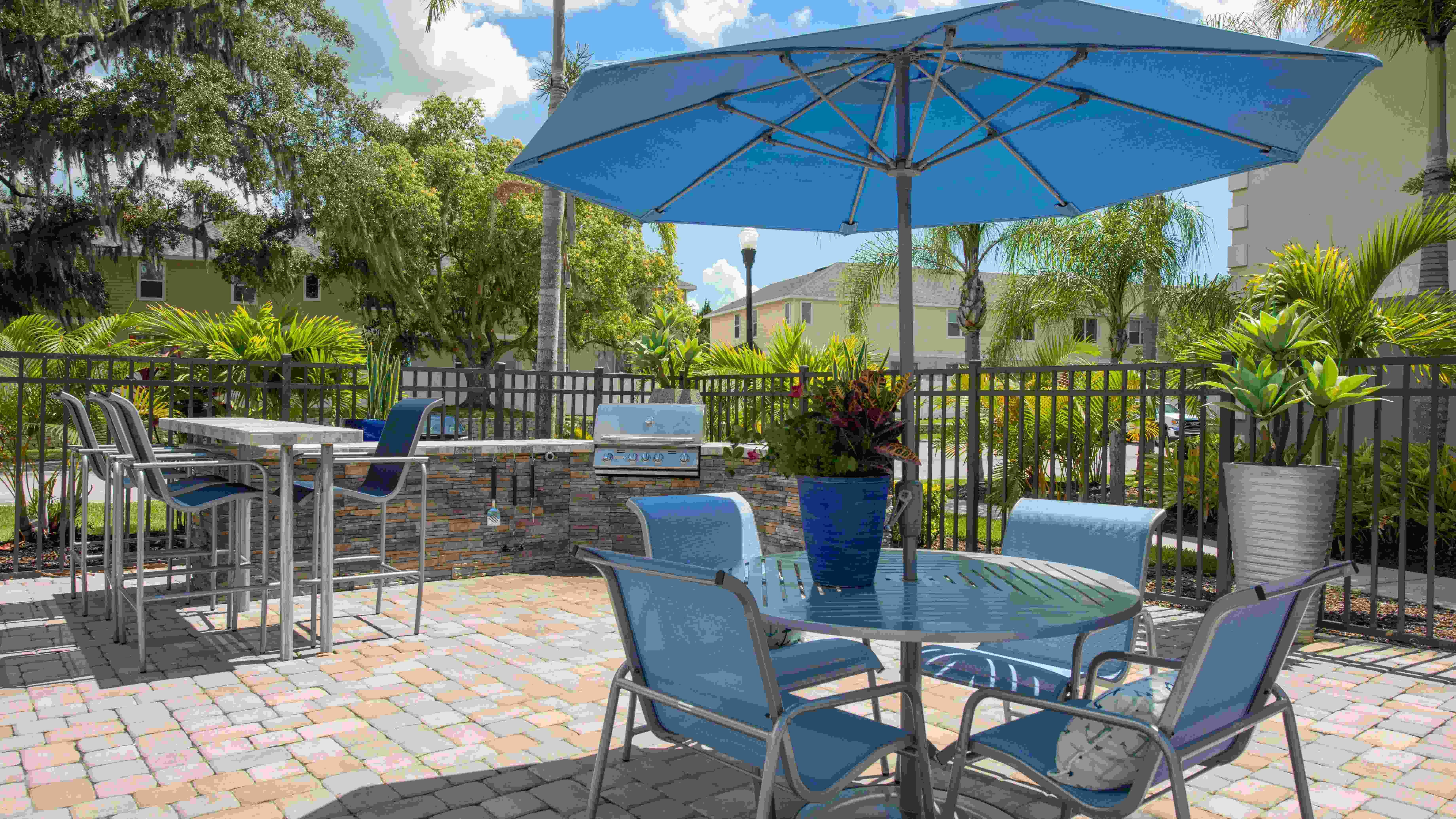 Enjoy outdoor dining at Soleil Blu Apartments in St Cloud, FL, featuring a modern outdoor kitchen with a gas grill, shaded seating, and beautiful landscaping, perfect for entertaining and relaxing.
