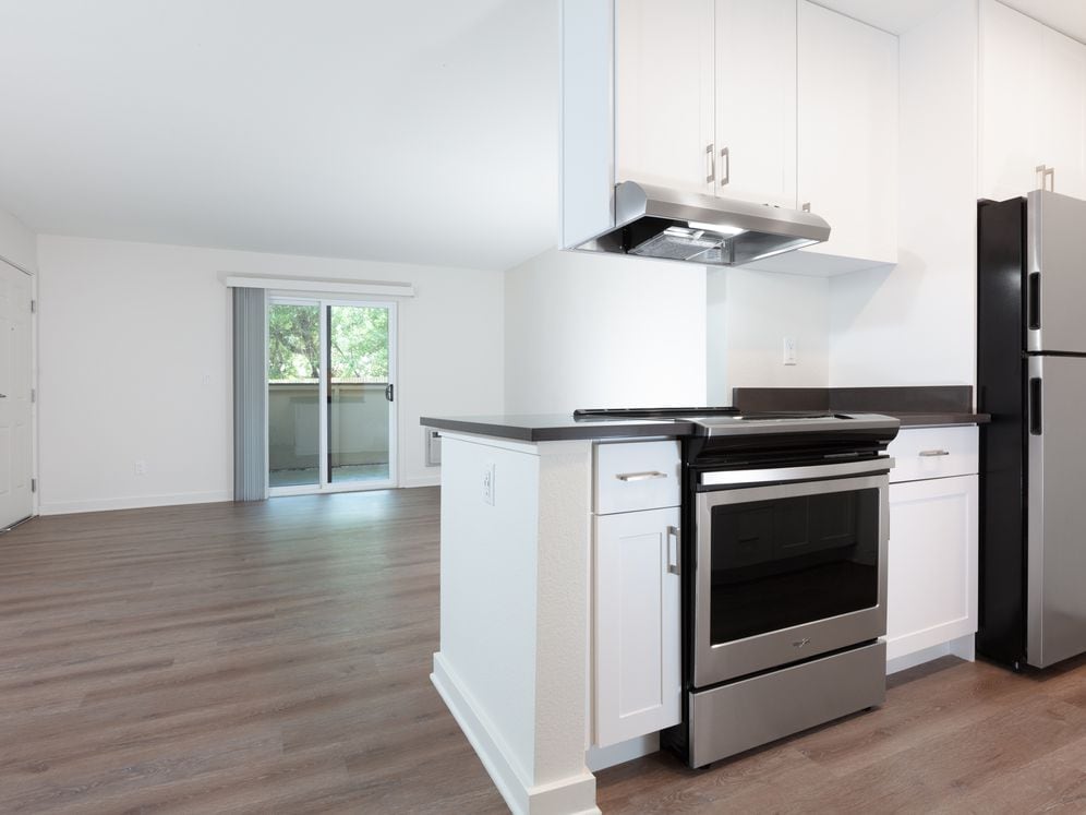Living area with balcony access and kitchen with white cabinetry, dark grey countertops, stainless steel appliances and hard surface flooring