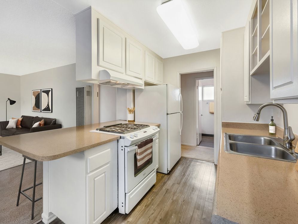 Classic Package I kitchen with white appliances, beige laminate countertops, white cabinetry, and hard surface flooring (select homes)