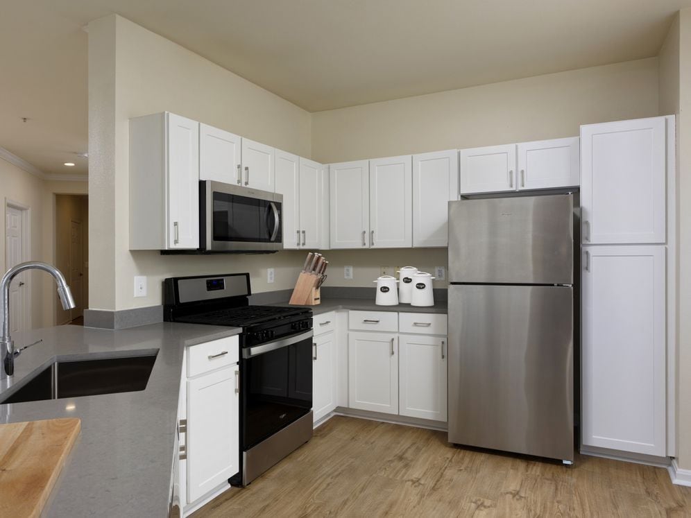 Renovated Package I kitchen with stainless steel appliances, grey quartz countertops, white cabinetry, and hard surface flooring