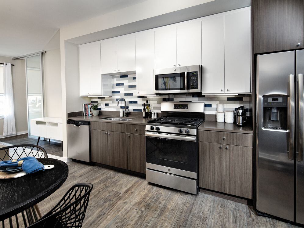 Modern Package kitchen with white and dark brown cabinetry, dark grey granite countertops, multi-colored subway tile backsplash, stainless steel appliances, and hard surface flooring