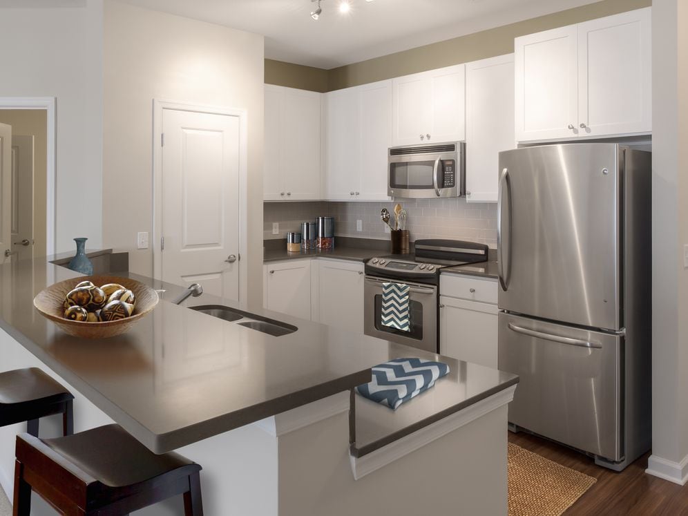 Kitchen with quartz stone countertop, white cabinetry, tile backsplash, stainless steel appliances and hard surface flooring
