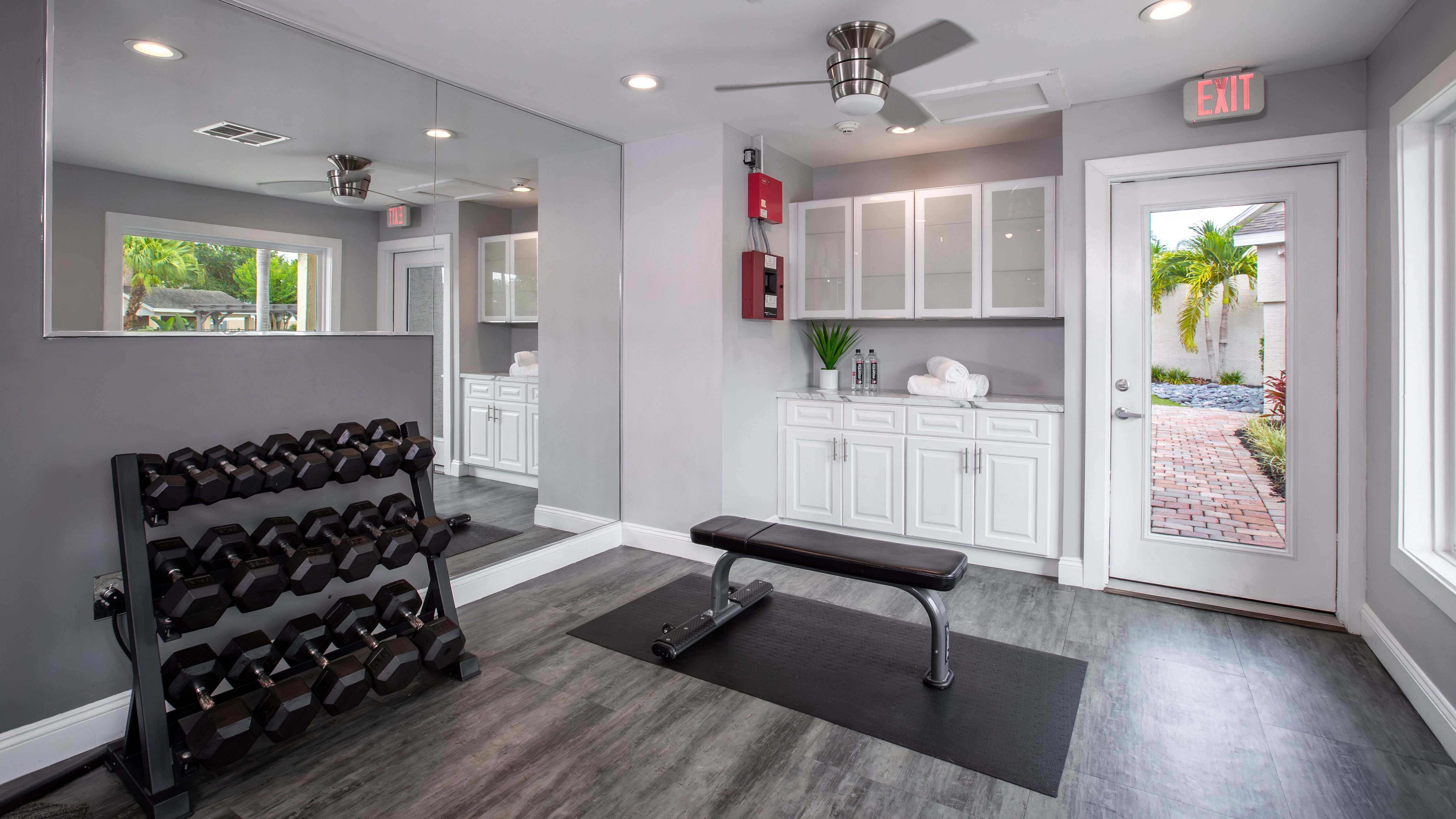 Harper Grand Apartments offers a dedicated weight room space featuring a full rack of dumbbells, a flat bench, and a peaceful outdoor view.