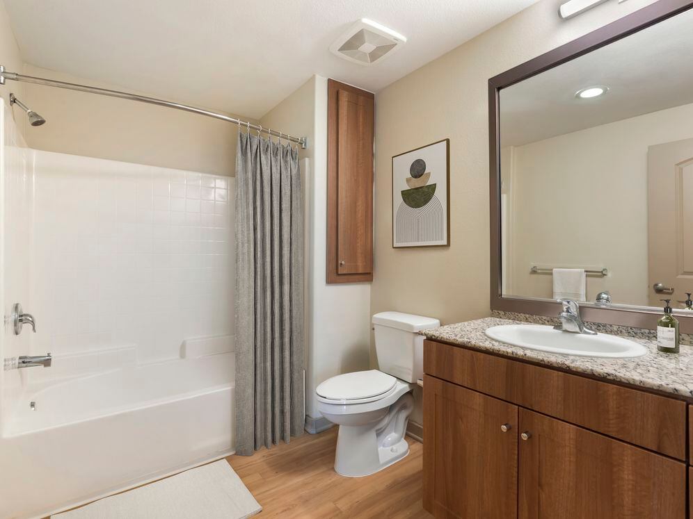 Updated Finishes bath with oak cabinetry, beige speckled granite countertops, and hard surface flooring