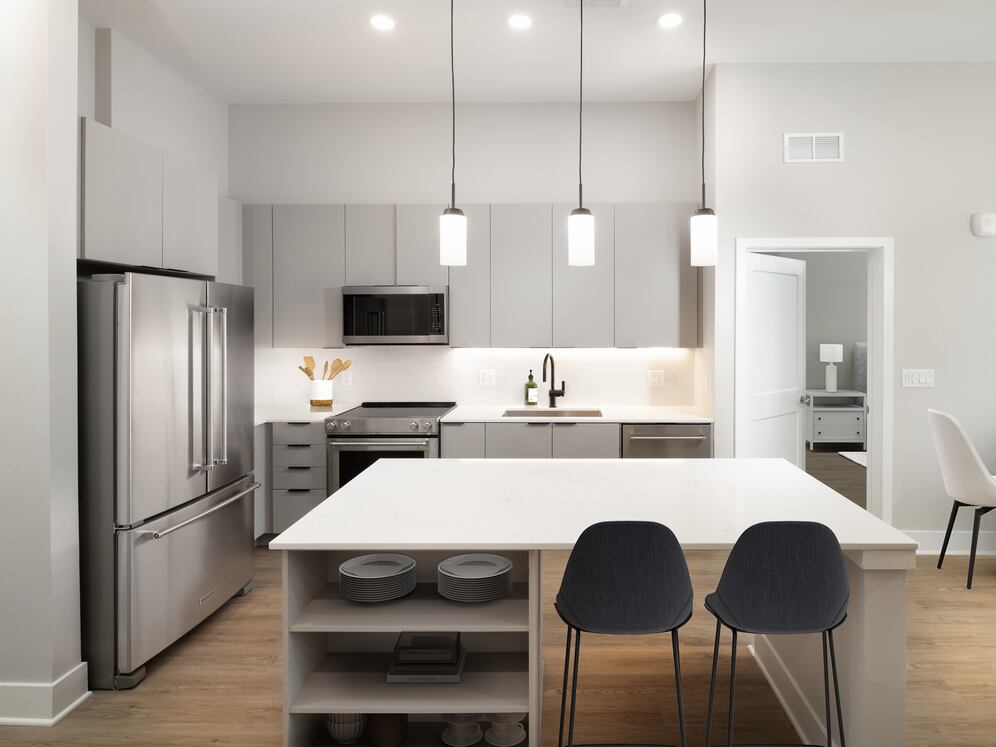 Signature Collection kitchen with stainless steel appliances, light grey cabinetry, marbled quartz countertops and backsplash, under-cabinet lighting, built-in shelves, and hard-surface flooring