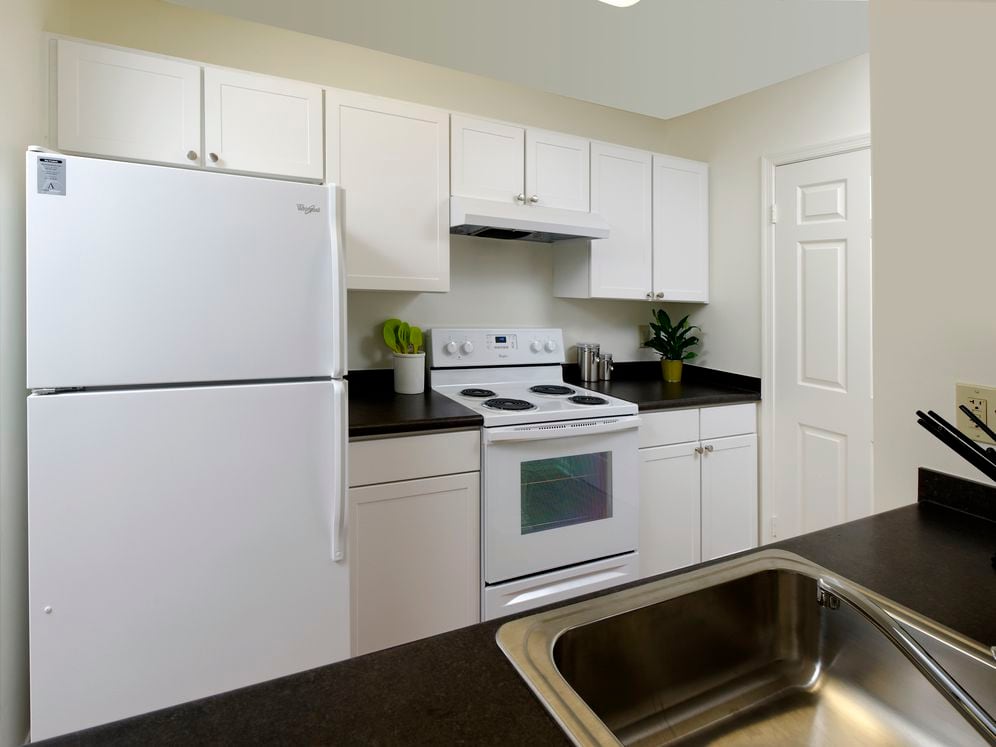 Kitchen with white appliances, white cabinetry and black countertops