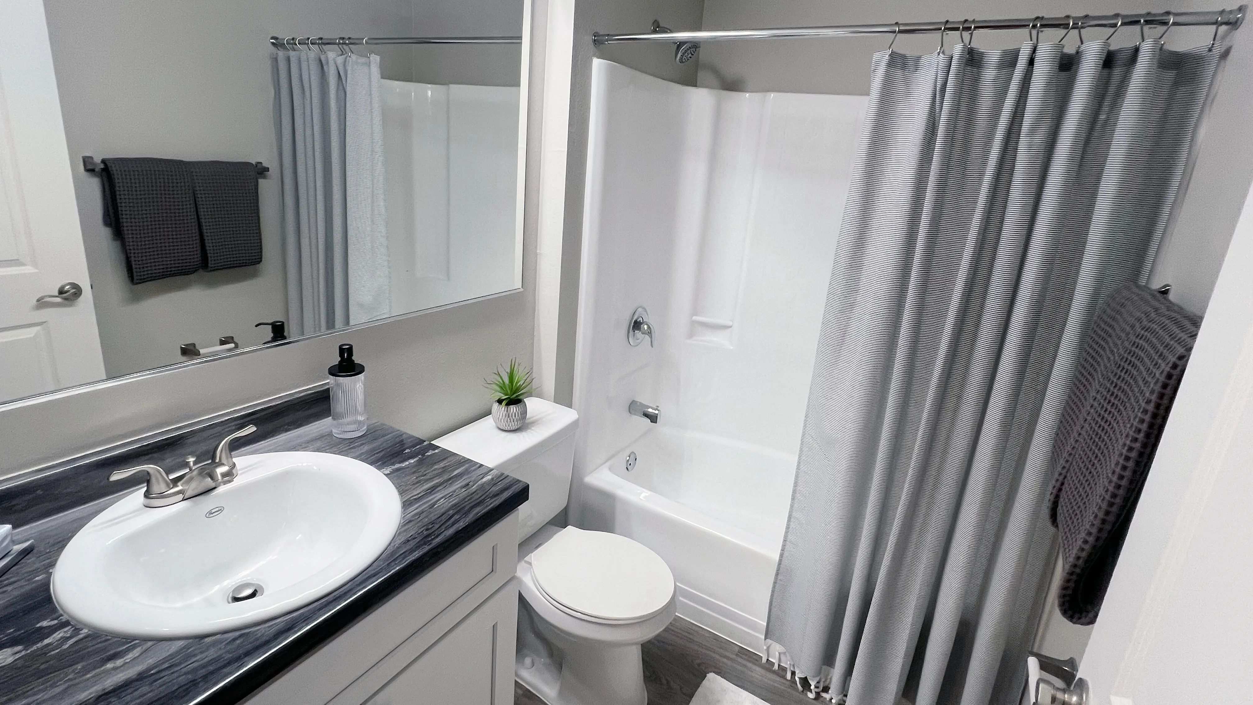 Modern bathrooms featuring black-fusion countertops, a spacious bathtub with a shower, and wood-style flooring.