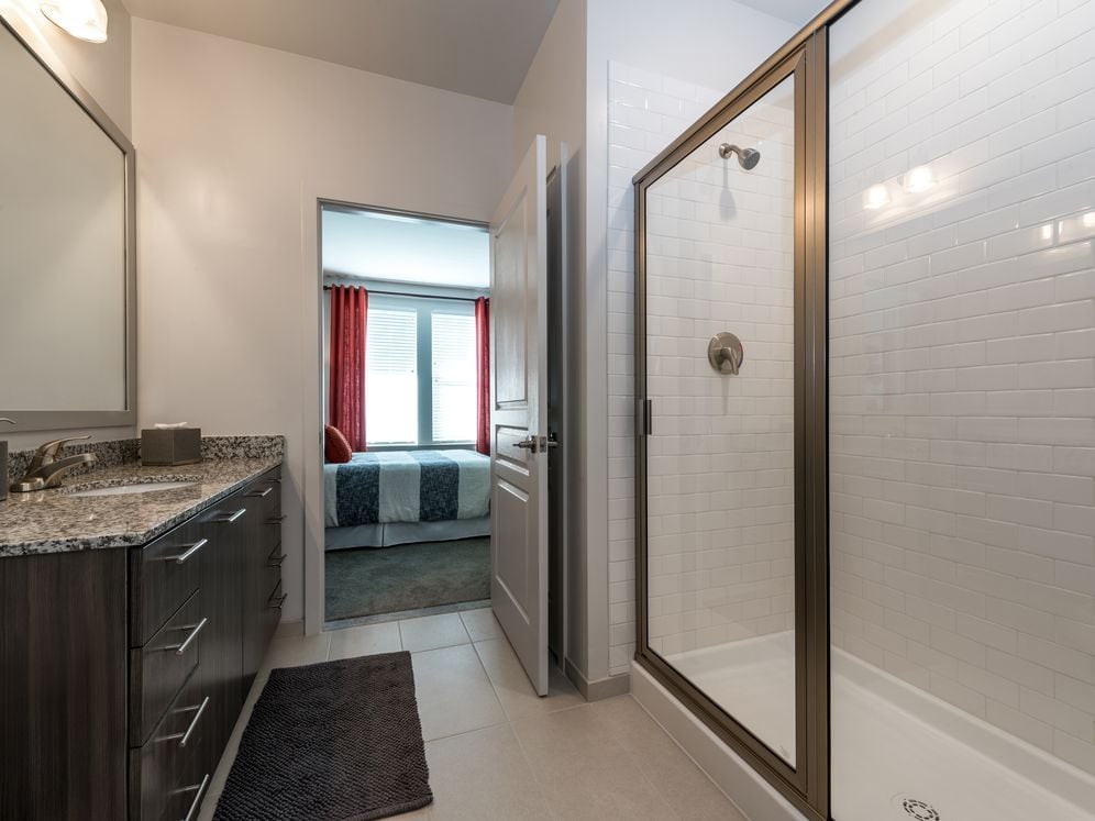 Bath with granite countertops, brown cabinetry, hard surface flooring and tiled shower