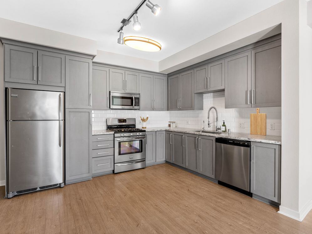 Kitchens with grey cabinetry, grey speckled granite countertops, white subway tile backsplash, stainless steel appliances, and hard surface flooring