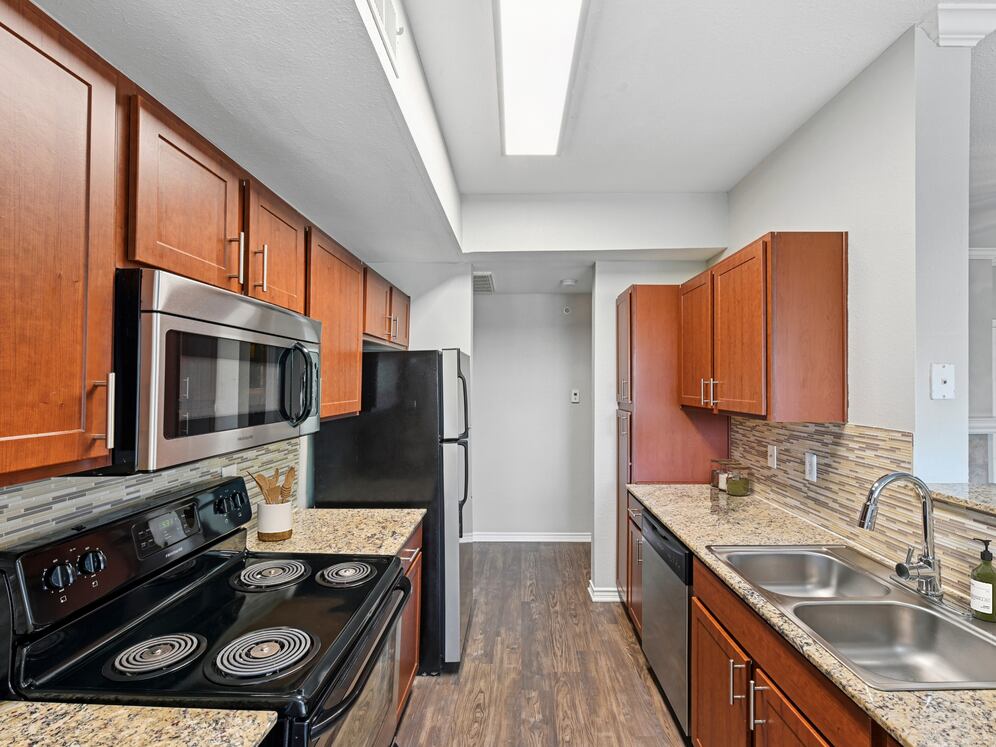Kitchen with chestnut cabinetry, speckled granite countertops, tile backsplash, stainless steel appliances, and hard surface flooring