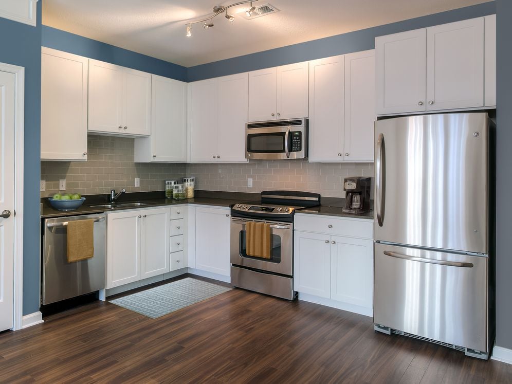 Kitchen with quartz stone countertop, white cabinetry, tile backsplash, stainless steel appliances and hard surface flooring.
