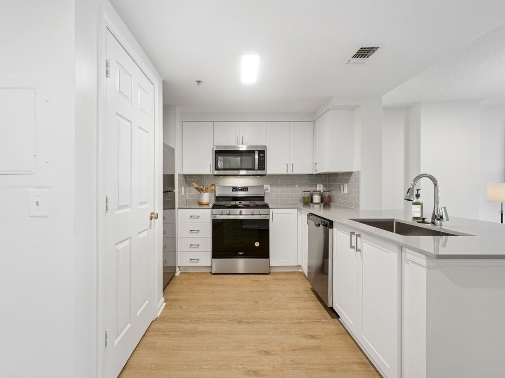 Renovated Package II kitchen with white cabinetry, grey quartz countertops, grey subway tile backsplash, stainless steel appliances, and hard surface flooring