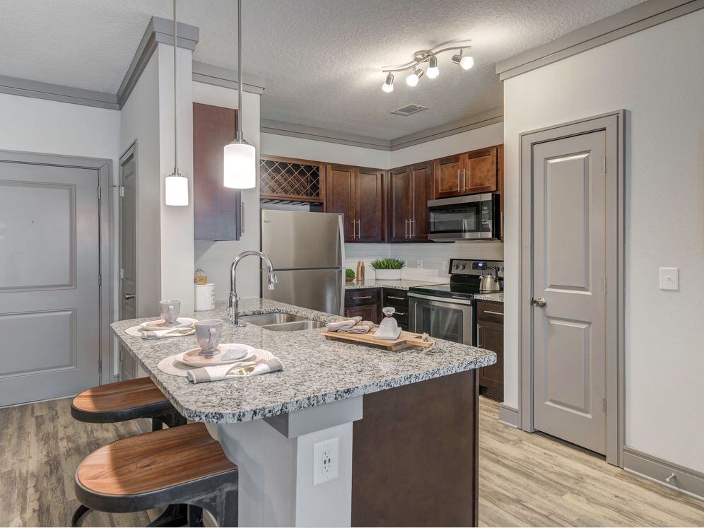 Modern kitchen with wood cabinetry, white tile backsplash, granite countertops, stainless steel appliances, and hard-surface flooring