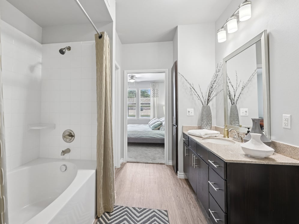 Bath with dark cabinetry, beige speckled granite countertops, and hard surface flooring