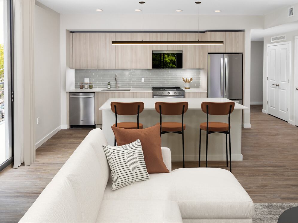 Upgrade Collection I Three-bedroom apartment kitchen with light wood cabinetry, grey tile backsplash, white quartz countertops, and stainless steel appliances