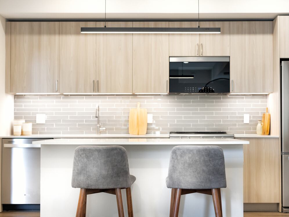 Upgrade Collection I kitchen with light wood cabinetry, grey tile backsplash, white quartz countertops, and stainless steel appliances