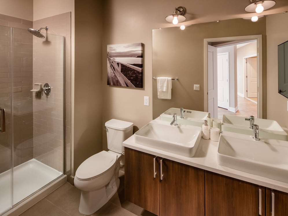 Signature Collection Bathroom with oak cabinetry light grey quartz countertops, white tile backsplash, and tile flooring
