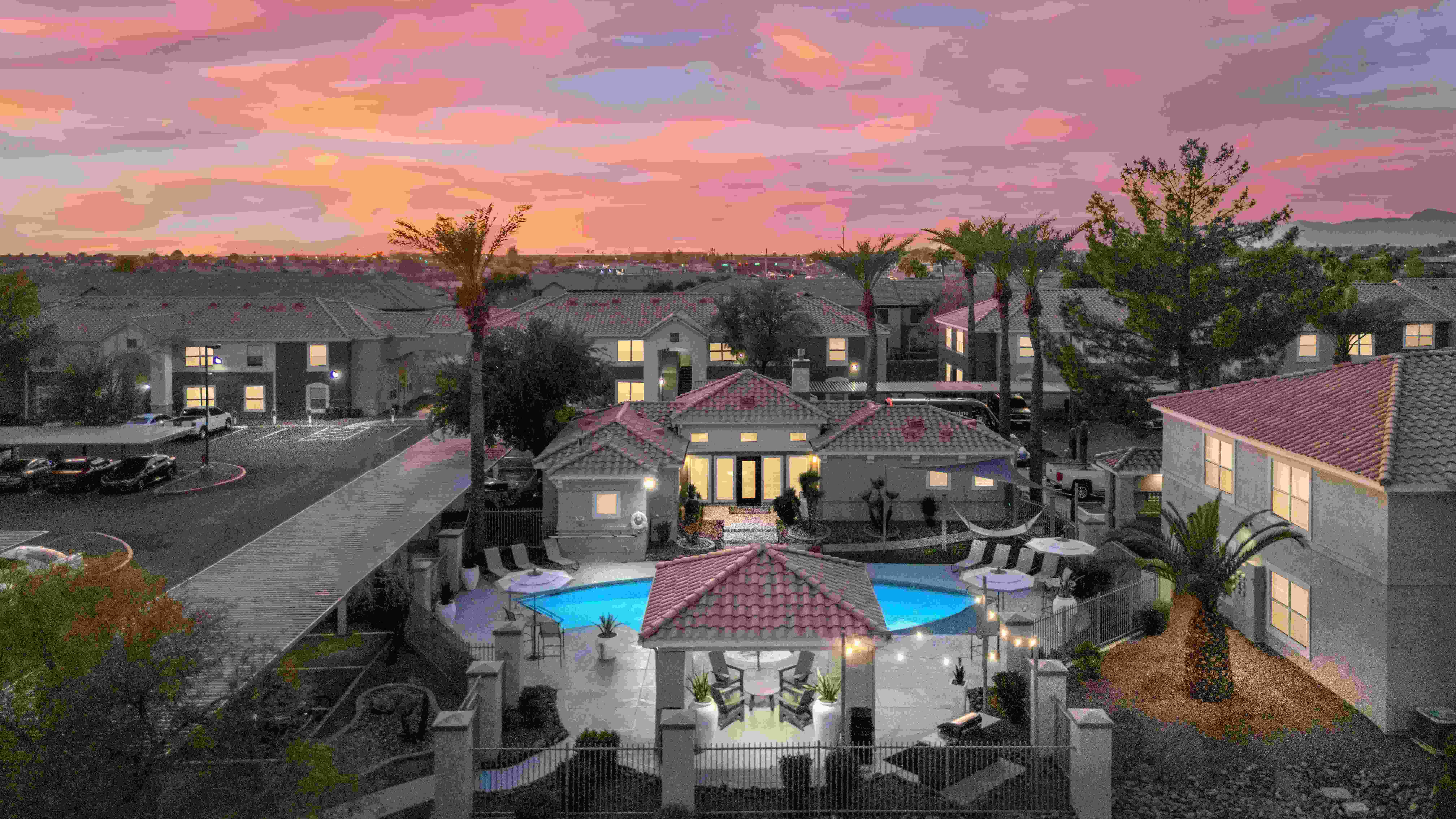 An enchanting aerial view of Sedona Peaks as the sun sets, casting a vibrant glow over the sky. The shimmering resort-style pool, elegant cabana seating, and palm-lined pathways create a serene escape, perfect for unwinding after a long day.