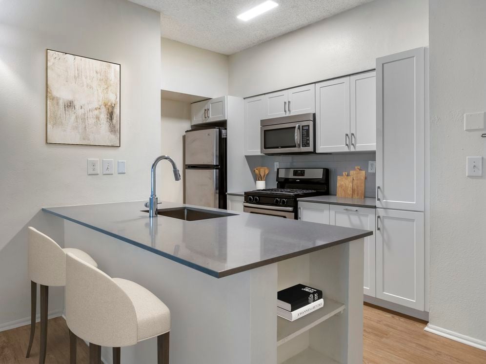 Renovated Package III kitchen with grey quartz countertops, white cabinetry, stainless steel appliances, tile backsplash, and hard surface plank flooring