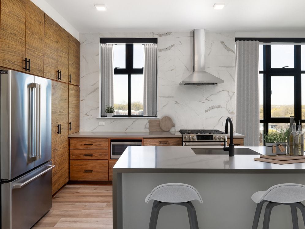 Kitchen with wood cabinetry, grey quartz countertops, marble backsplash, stainless steel appliances, and hard surface flooring