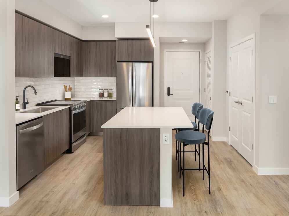 Upgrade Collection II One-bedroom kitchen with espresso cabinetry, white tile backsplash, stainless steel appliances, and hard-surface vinyl plank flooring