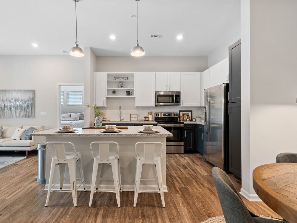 Kitchen with white and dark cabinetry, speckled granite countertops, white subway tile backsplash, stainless steel appliances, and hard surface flooring