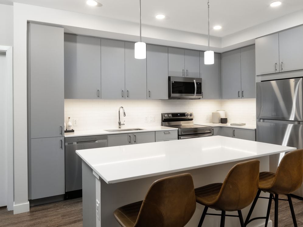 Base Collection kitchen with stainless steel appliances, white quartz countertops, white tile backsplash, dark grey cabinetry, and hard surface flooring (representative imagery)