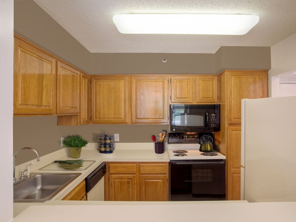 Kitchen with oak cabinetry, beige countertops and black appliances