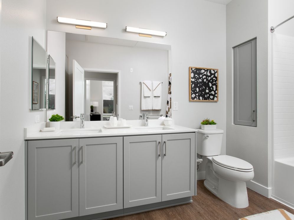 Apartments with modern baths featuring grey cabinetry, white quartz stone countertops, and hard surface flooring