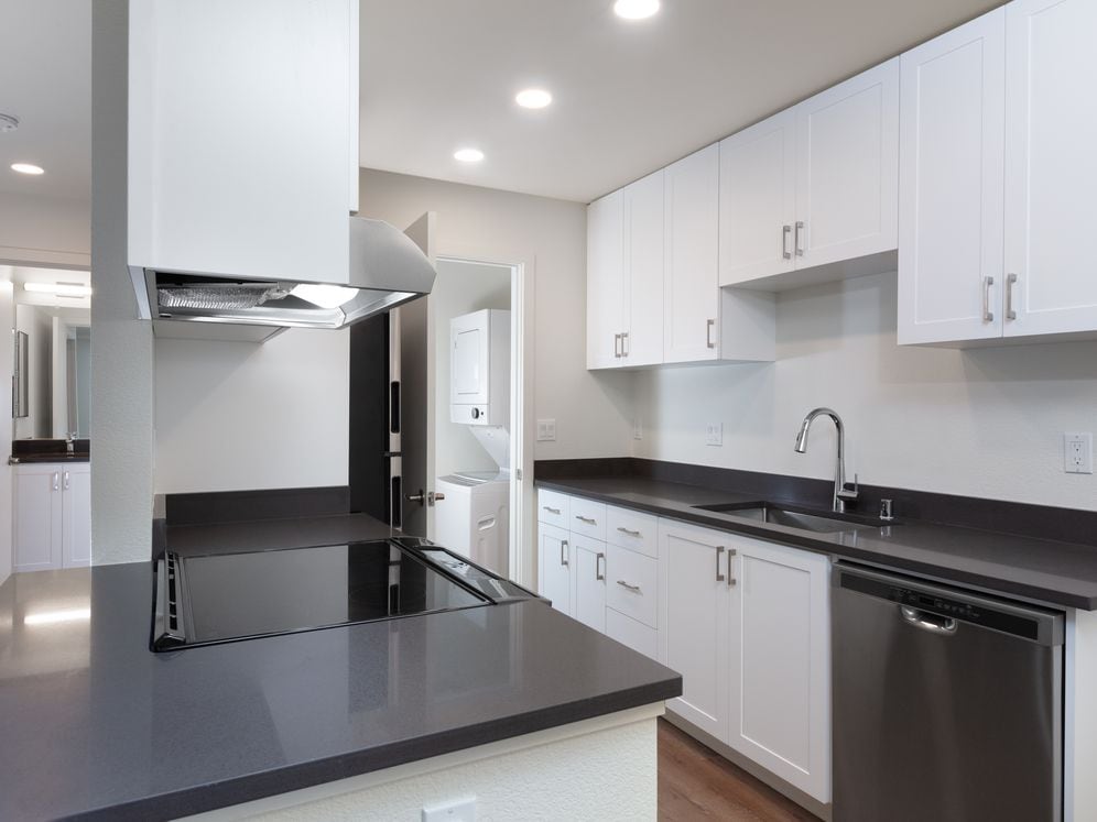 Kitchen with white cabinetry, stainless steel appliances, dark grey countertops and hard surface flooring